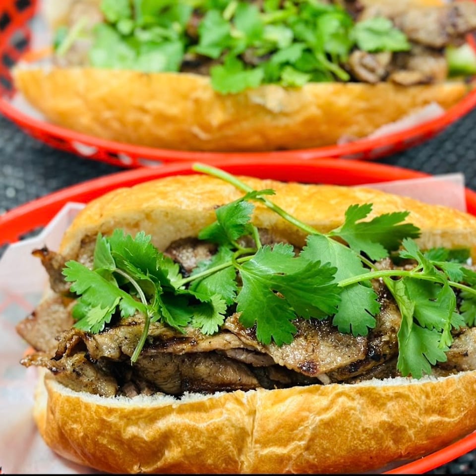 Two grilled pork banh mi sandwiches with cilantro in red baskets.