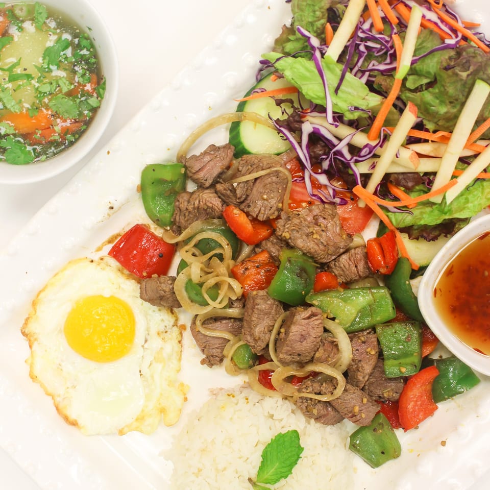 Stir-fried beef with bell peppers, onions, rice, fried egg, salad, soup, and dipping sauce.