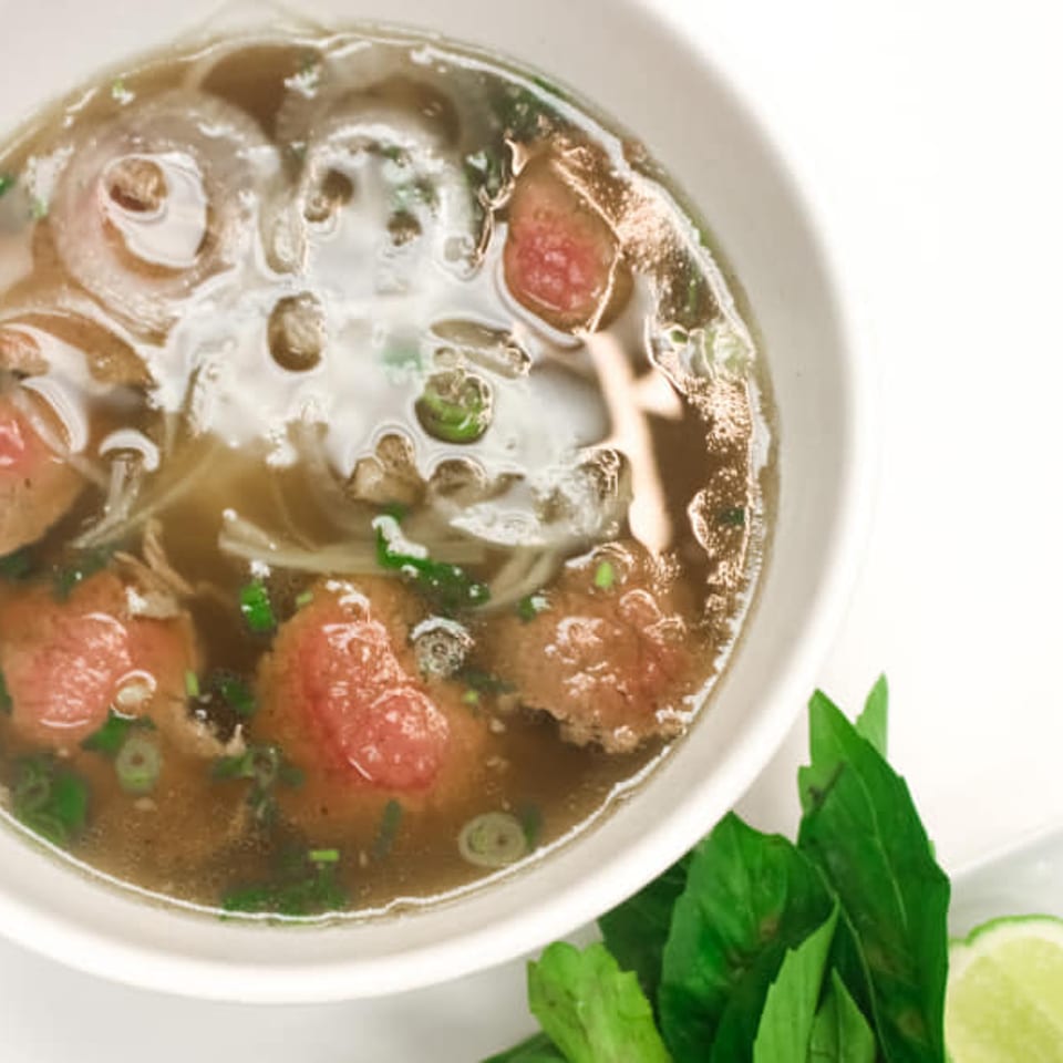 Bowl of pho with beef, noodles, and broth, garnished with fresh basil and lime.
