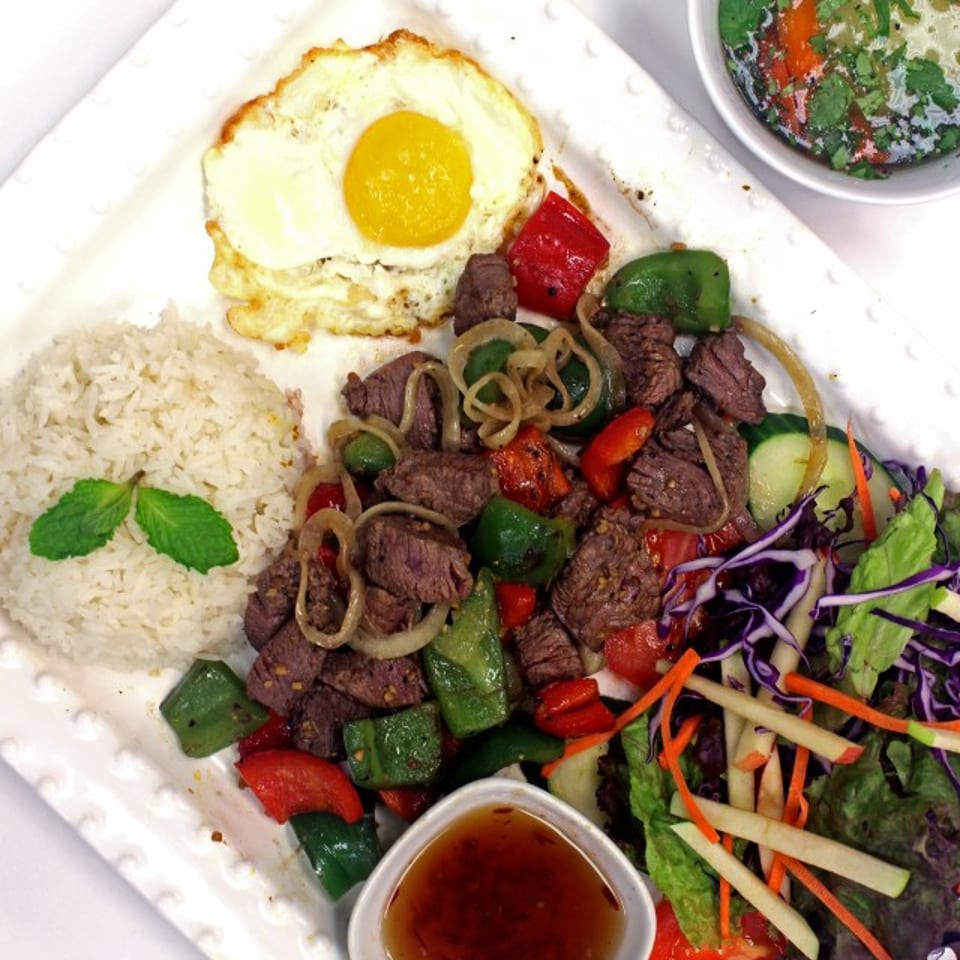 Shaking beef with rice, fried egg, salad, and a side of soup on a white plate.