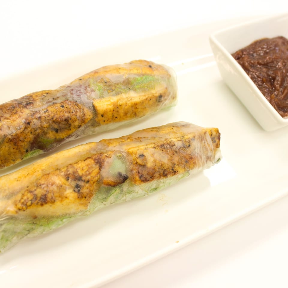 Two spring rolls with chicken and vegetables, served with a side of dark dipping sauce.