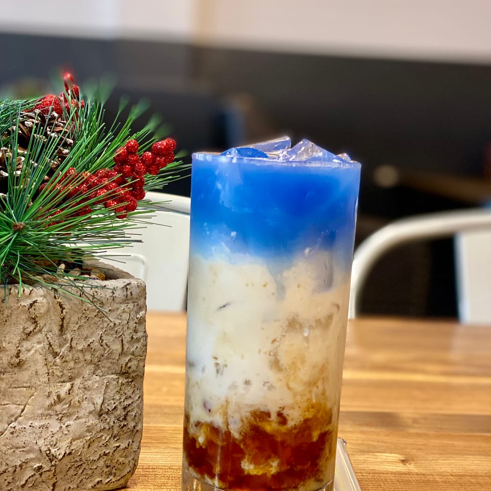 Layered blue, white, and red drink with ice, next to a festive pine and berry decoration.