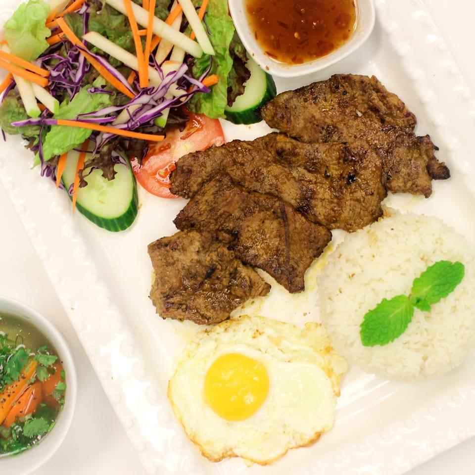 Grilled pork, fried egg, rice, salad, and soup on a white rectangular plate.